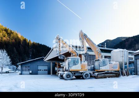 Vue panoramique pelles hydrauliques gelées debout à l'extérieur conditions hivernales couvert de glace enneigée bâtiment industriel zone alpine. Impacts par temps froid Banque D'Images