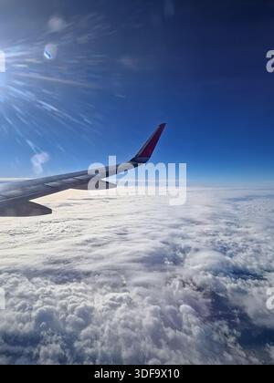 Vol en avion au-dessus des nuages. Horizon bleu et aile d'avion vus par la fenêtre Banque D'Images