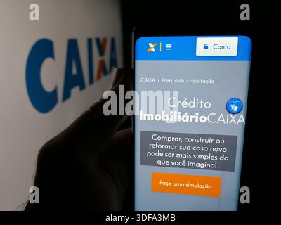 Dans cette illustration photo, une personne tient un smartphone avec la page Web de la Caixa Economica Federal (CEF) brésilienne sur l'écran devant le logo. Banque D'Images