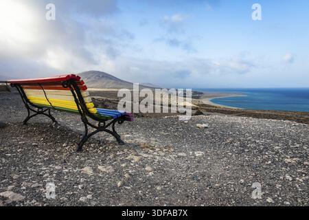 Un banc vide, peint dans un arc-en-ciel de couleurs et une vue sur Playa de Sotavento de Jandia. Fuerteventura. Îles Canaries. Espagne Banque D'Images