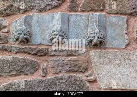 Trois reliefs de tête de lion anciens décorent un mur près de l'église Hagia Eleni à Sille près de Konya, en Turquie – probablement des spolia réutilisées d'une structure antérieure. La surface en grès érodée du mur environnant souligne le grand âge du site. Banque D'Images