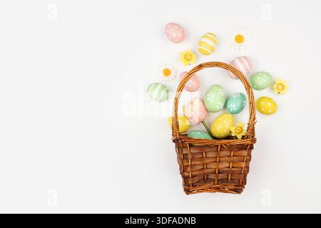Renversement panier de Pâques d'oeufs de Pâques et de fleurs colorés peints à la main pastel. Vue de haut en bas sur un fond blanc. Banque D'Images