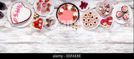 Bordure supérieure de la Saint-Valentin avec une variété de desserts et de bonbons. Vue aérienne sur un fond de bannière en bois blanc. Thème amour et coeurs. Copier l'espace. Banque D'Images