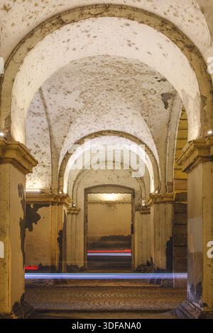 Photo longue exposition d'un couloir historique voûté en décomposition avec peinture écaillée, taches de moisissure et traînées de lumière spectaculaires provenant de véhicules qui passent. Sélect. F Banque D'Images