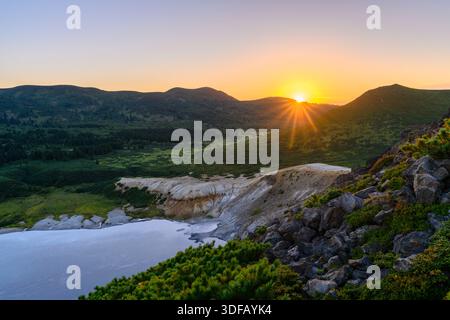 La lumière dorée du soleil se répand sur les collines, illuminant le terrain serein de la région éloignée de la Russie. Un lac tranquille reflète le ciel vibrant tout en natur Banque D'Images