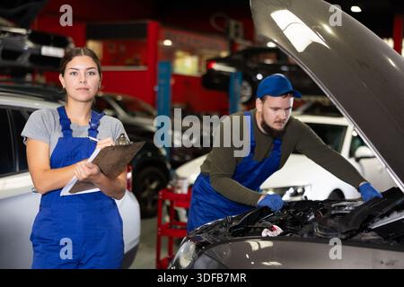 Travailleuse de service automobile tient des registres du travail effectué par les mécaniciens automobiles dans la station-service automobile - prend des notes sur papier Banque D'Images