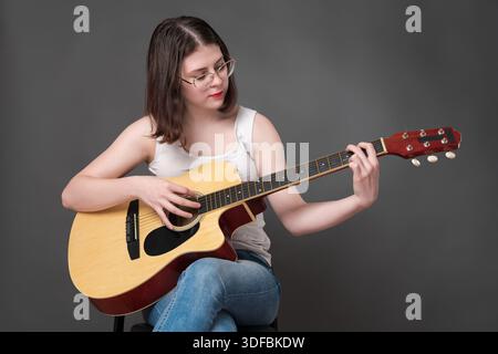 Femme guitariste jouant de la guitare classique acoustique et regardant la corde. Jeune joueuse de guitare européenne adulte, appartenant à la génération Z, portant Banque D'Images