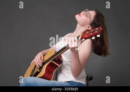Femme guitariste interprète des morceaux de musique avec passion et talent, en utilisant de manière impressionnante la guitare acoustique. Musicienne portant des lunettes les yeux fermés. BT Banque D'Images