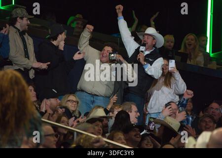 Un groupe de personnes assis dans le stade, certains acclamant les bras levés, avec un homme dans un chapeau de cow-boy tenant un micro. Banque D'Images