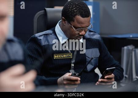 Homme noir d'âge moyen surveillant les dispositifs de sécurité lorsqu'il est assis à l'intérieur Banque D'Images