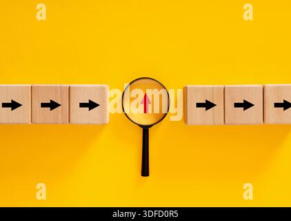 La loupe se concentre sur la flèche rouge vers le haut parmi les flèches horizontales noires sur fond jaune, la pensée différente et la recherche de nouvelles opportunités Banque D'Images