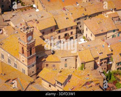 Vue aérienne des toits baignés de soleil et de l'emblématique tour de l'horloge projetant des ombres sur les rues anciennes, Pienza, Toscane, Italie. Banque D'Images