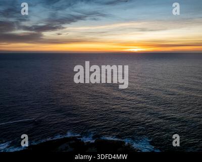 Vue aérienne des eaux sombres de l'océan rencontrer le ciel enflammé avec des teintes flamboyantes au coucher du soleil, peignant un panorama à couper le souffle sur l'horizon, Kiama, New SO Banque D'Images