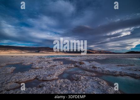 Plan grand angle haute résolution de formations salines et de piscines minérales sous un ciel crépusculaire spectaculaire et nuageux dans un paysage désertique. Banque D'Images