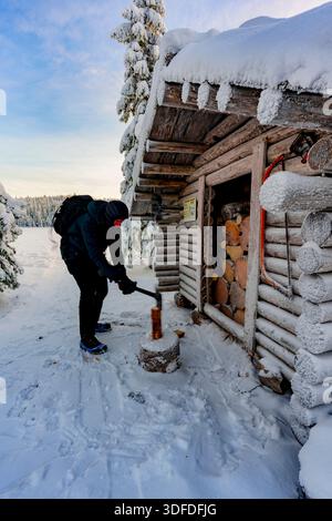 Homme coupant du bois à l'extérieur d'une cabane enneigée Banque D'Images