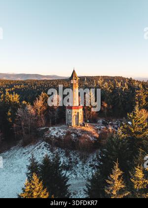 La tour de guet Stepanka se dresse dans les montagnes de Jizera pendant l'hiver. La lumière du soleil brille sur la tour entourée d'arbres enneigés et de montagnes en arrière-plan. Banque D'Images