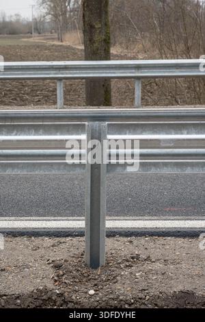 Gros plan d'un nouveau garde-corps en métal et d'un poteau de soutien sur une route rurale nouvellement construite en Allemagne, mettant l'accent sur la symétrie, la texture et la structure linéaire. Banque D'Images