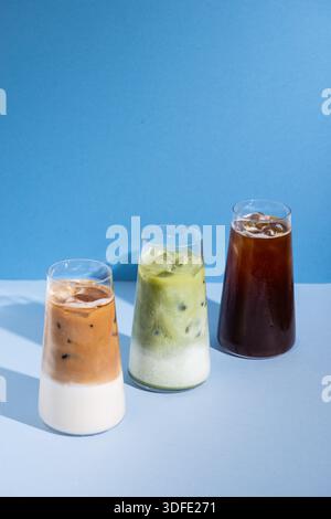 Trois boissons glacées servies dans des verres transparents sur un fond de studio propre et minimal, y compris un latte matcha, un café glacé et un latte glacé. Banque D'Images