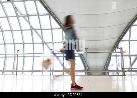 Une femme marche dans la région de flou au couloir blanc avec de grandes fenêtres. Les personnes qui s'estompent dans un bâtiment moderne. Image abstraite de voyageur dans le lo Banque D'Images