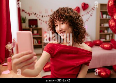 Portrait de jeune femme adulte souriant tout en prenant Selfie à l'intérieur Banque D'Images