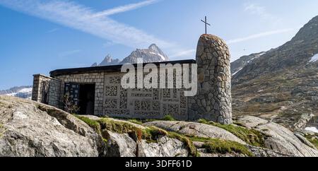 Une petite chapelle en pierre avec une croix sur une colline rocheuse, entourée de montagnes. Banque D'Images