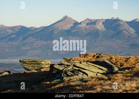 Vue sur les roches déchiquetées et les herbes dorées rencontrent la chaîne de montagnes lointaine et brumeuse sous un ciel clair, Stredna hola, Banskobystricky kraj, Slovaquie. Banque D'Images