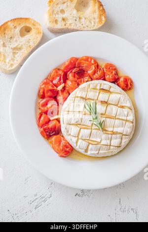 Fromage crémeux servi avec des toasts et des tomates juteuses sur fond blanc vif Banque D'Images