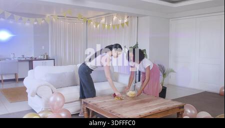 Penchant deux femmes organisant des collations sur la table du salon, plaçant un bol en verre, portant des vêtements décontractés Banque D'Images