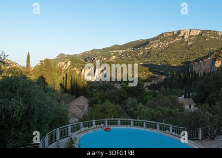 Vue depuis un balcon dans la station touristique un matin, piscine vide ci-dessous, première lumière du soleil sur les arbres et les montagnes au loin Banque D'Images
