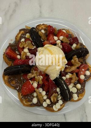 Vue de dessus d'un délicieux dessert à base de gaufres belges servi sur une assiette blanche, garni de fraises fraîches tranchées, de pâte à tartiner au chocolat, de biscuits Oreo, de Banque D'Images