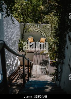 Vue verticale des escaliers et des chaises de patio vides dans une cour ensoleillée avec de fortes ombres. Banque D'Images