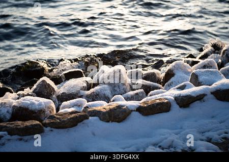 Glace sur la surface de pierre au bord d'un lac. Gros plan d'eau gelée rétroéclairée par le soleil. La glace forme une couche de revêtement externe. Banque D'Images