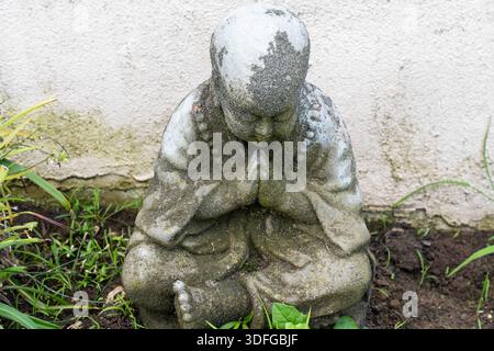 Statue en pierre altérée de Bouddha est assis dans la méditation tranquille. Mains pressées, tête courbée, yeux fermés. Banque D'Images