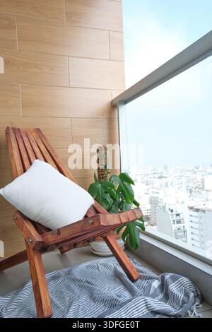 Espace de balcon urbain confortable avec une chaise en bois, une plante tropicale et la ligne d'horizon de la ville Banque D'Images