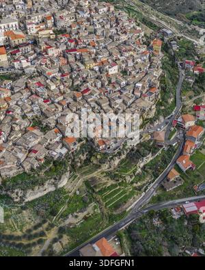 Vue aérienne de l'ancienne ville accrochée à la colline escarpée, toits en terre cuite contrastant avec les bâtiments en pierre pâle, Agira, Sicile, Italie. Banque D'Images