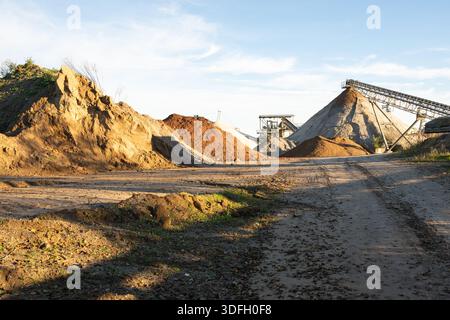 Site de traitement de gravier avec de grands tas de sable et des systèmes de convoyage dans un paysage industriel ouvert sous un ciel nocturne d'automne dans le sud de l'Allemagne. Banque D'Images