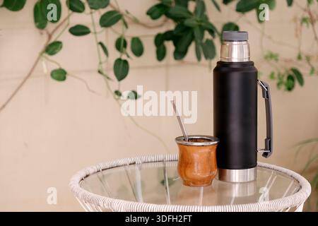 Thermos et tasse de maté en bois avec paille. Dans la cour arrière au-dessus d'une table en verre. Yerba Mate, boisson chaude traditionnelle sud-américaine. Banque D'Images