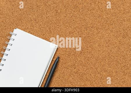Photo macro d'un cahier blanc et d'un stylo noir en bas à gauche de l'écran sur un fond de liège Banque D'Images