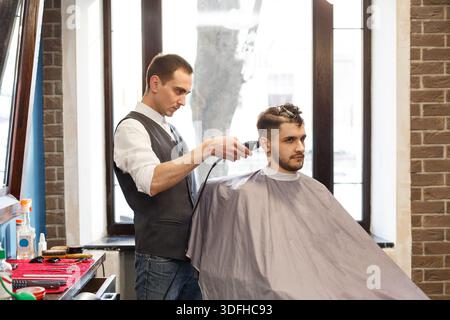 Homme se faisant couper les cheveux par coiffeur au salon de coiffure Banque D'Images