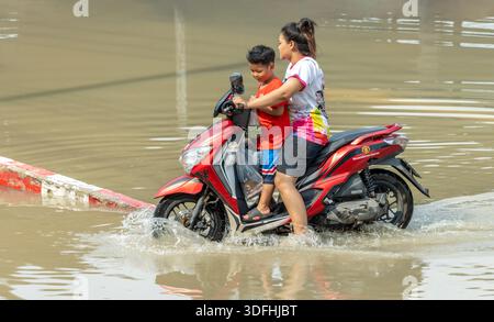 BANGKOK, THAÏLANDE, nov 09 2025, mère et enfant conduisent une moto dans une rue inondée Banque D'Images