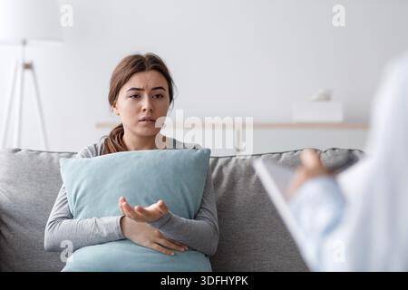 Triste malheureux bouleversé jeune femme européenne assise sur un canapé serrant l'oreiller et parlant à un psychologue au bureau Banque D'Images