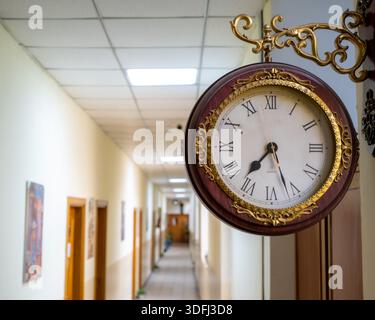 Une horloge murale vintage avec des chiffres romains accrochés dans un couloir, un éclairage doux, un cadre en bois, un couloir flou en arrière-plan Banque D'Images