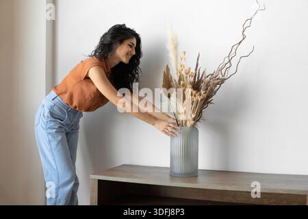 Décoration intérieure moderne et minimaliste. Jeune femme organisant des plantes séchées dans un vase, créant une atmosphère chaleureuse dans la maison Banque D'Images