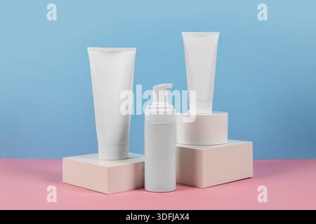 Beaux modèles cosmétiques pour les annonces, tubes de crème en plastique et bouteilles sur un fond bleu avec des podiums. Design esthétique pour un produit haut de gamme Banque D'Images