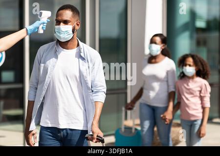 Travailleur médical vérifiant la température corporelle de l'homme noir à l'aéroport Banque D'Images