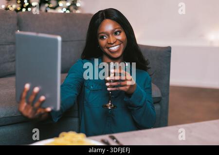 Femme appréciant boire tout en prenant Selfie à la maison pendant la réunion du soir Banque D'Images