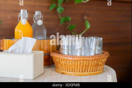 Verres vides mis dans un panier en osier avec jus d'orange et eau en bouteille, boîte de mouchoirs au bar buffet. Banque D'Images