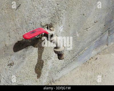 Le Caire, Egypte, 6 janvier 2026 : robinet d'eau métallique avec une poignée rouge, monté sur un mur de béton rugueux Banque D'Images