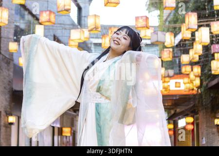 Vue d'une femme souriante en robe traditionnelle Hanfu, bras tendus au milieu de lanternes incandescentes dans les ruelles de Guilin, Guangxi, Chine. Banque D'Images