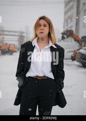 Portrait de femme avec tache de Porto-vin portant un costume noir. Femme réussie posant dans les chutes de neige d'hiver contre le fond industriel urbain. E Banque D'Images
